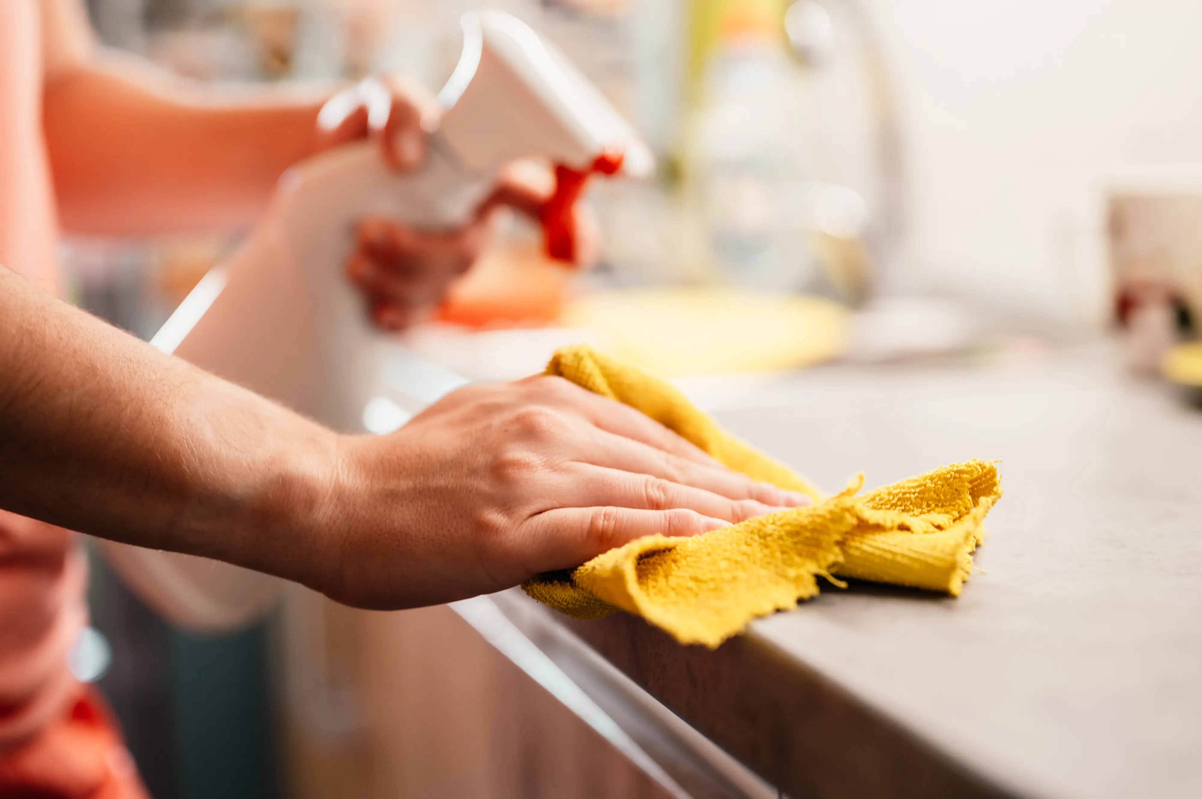 Pessoa higienizando uma mesa utilizando um pano e um borrifador